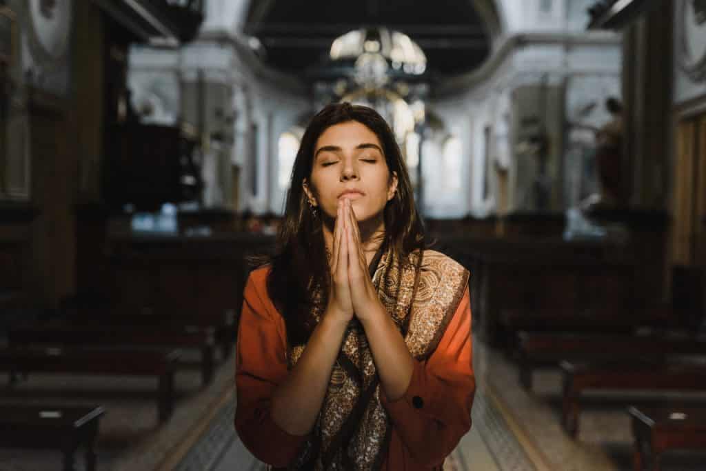Uma mulher ajoelhada rezando de olhos fechados. 