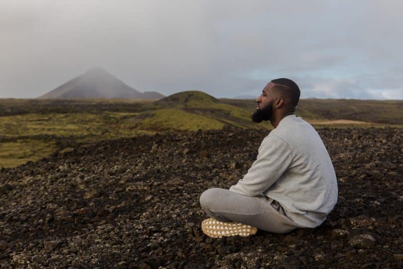 Homem sentado em um chão de terra olhando para o horizonte