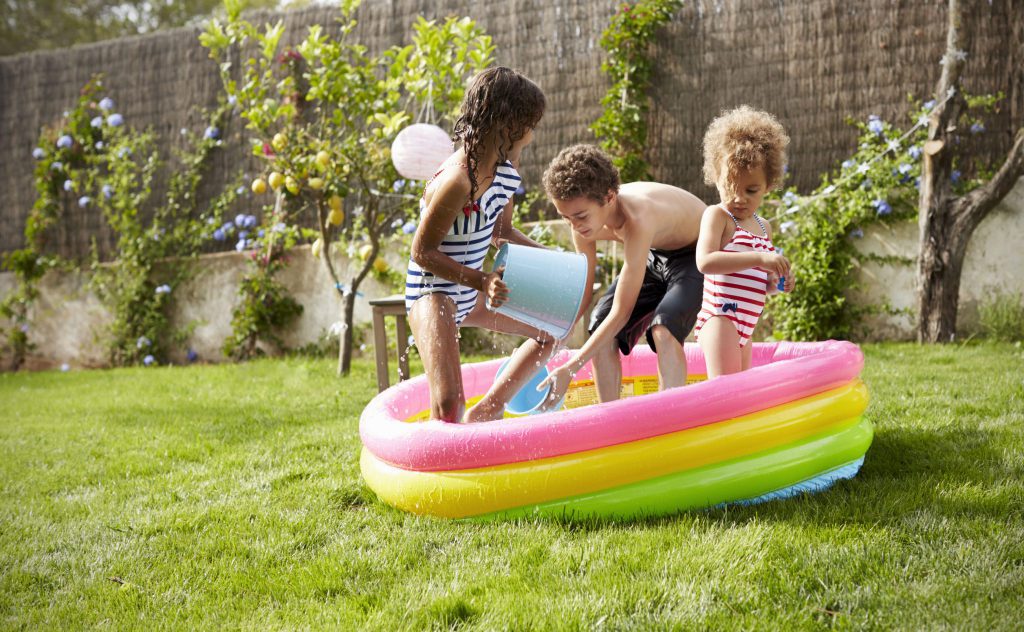 Três crianças brincando em uma piscina de plástico no quintal.