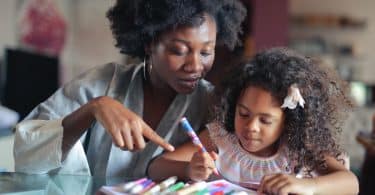 Criança pintando ao lado de uma mulher