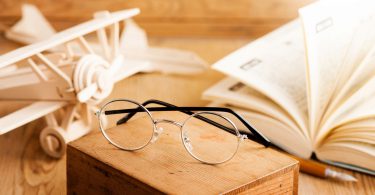 Óculos redondos, livro aberto e avião de madeira.