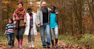 Família formada por um homem e mulher brancos, com 3 crianças negras, caminhando em meio a natureza.