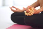 Recorte das mãos de uma mulher meditando e segurando um japamala.