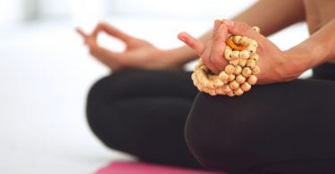 Recorte das mãos de uma mulher meditando e segurando um japamala.