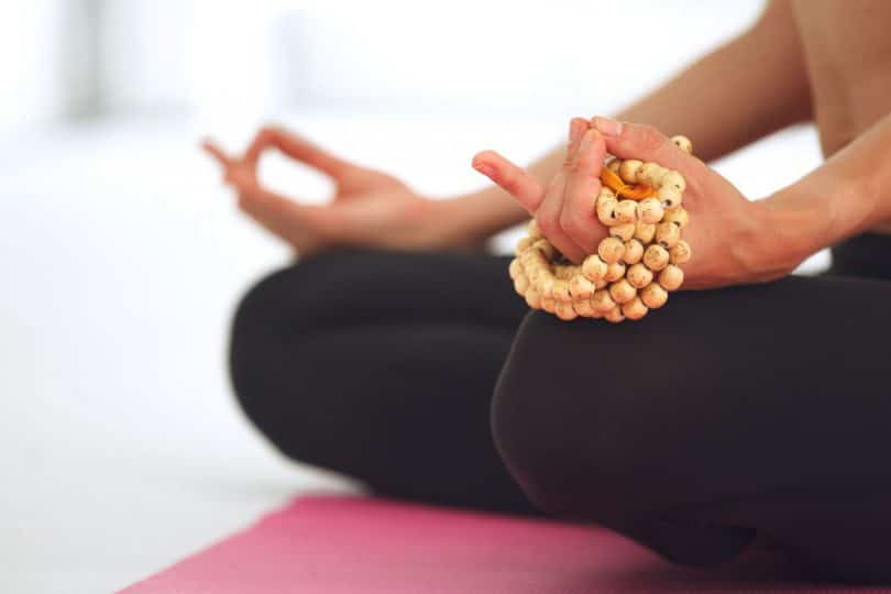 Recorte das mãos de uma mulher meditando e segurando um japamala.
