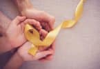 Mãos de uma criança em cima de uma mão de um adulto segurando fita amarela