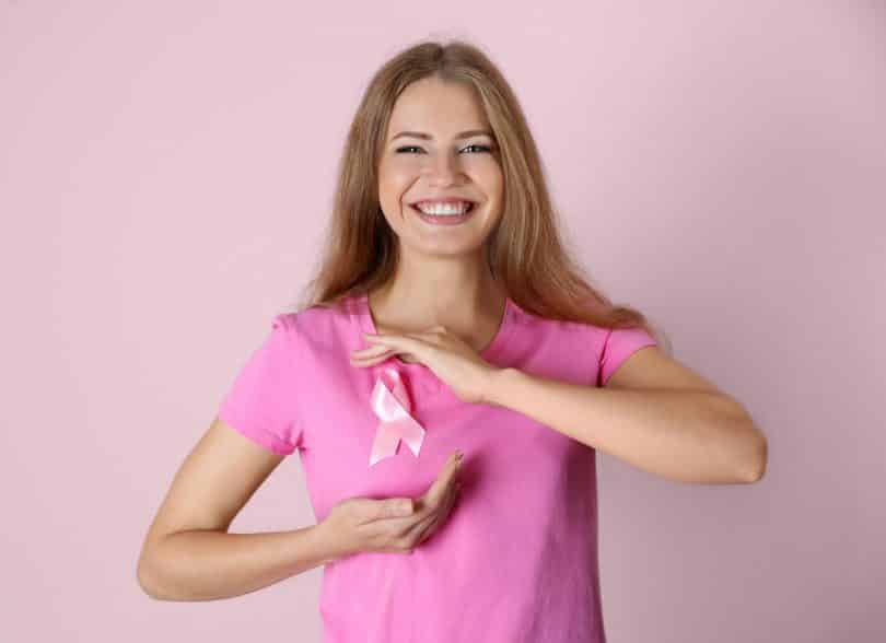 Mulher com as mãos sobre o peito, ao redor de uma faixa que simboliza a luta contra o câncer de mama.