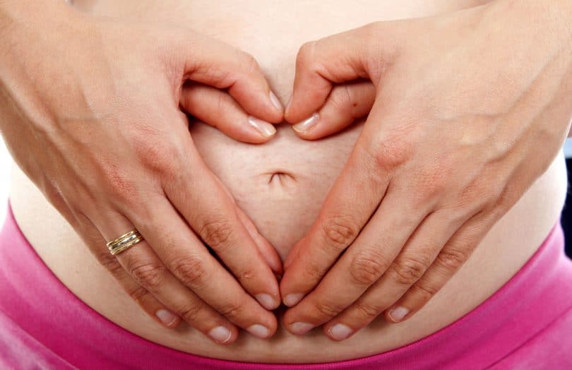 Barriga de grávida, com dois pares de mãos em cima, um masculino e um feminino, formando um coração.
