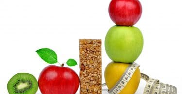 Frutas juntas, maçãs, kiwis, peras, perto de uma barrinha de cereal e uma fita métrica.
