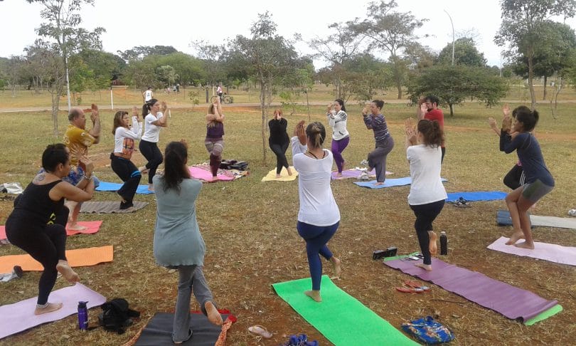 Grupo de pessoas em um parque, organizadas em circulo, praticando ioga.