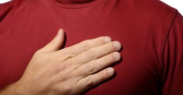 Homem vestindo camiseta vermelha, com a mão direita sobre o coração.