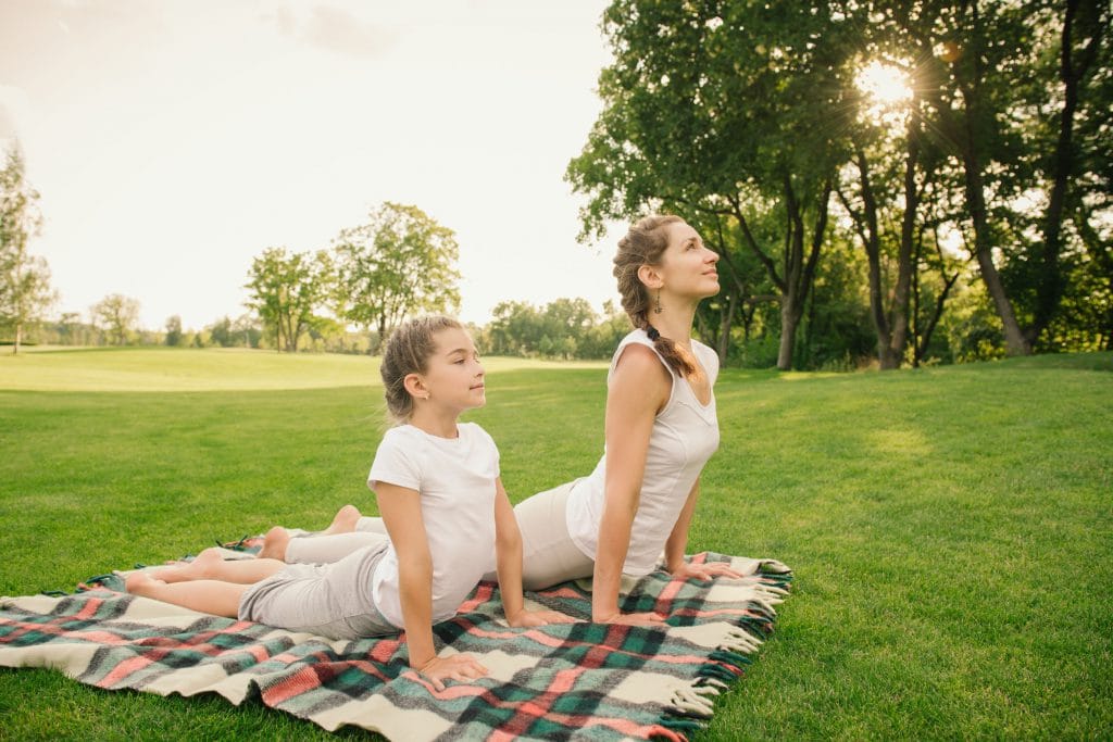 Mãe e filha fazendo yoga em um parque aberto.