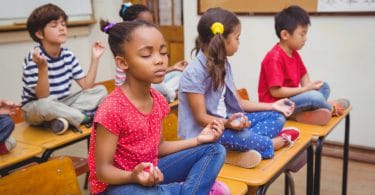 Crianças em posição de meditação em cima de suas mesas escolares.
