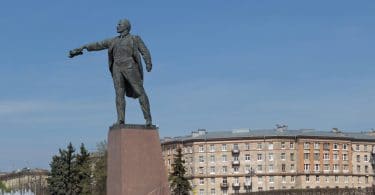 Estátua de homem baixinho, dando uma ordem com a mão, em cidade antiga.