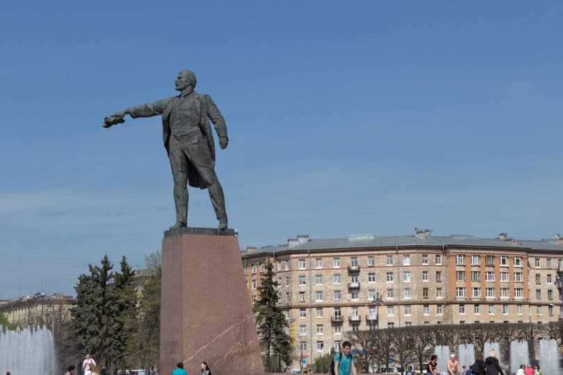 Estátua de homem baixinho, dando uma ordem com a mão, em cidade antiga.