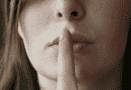 Mulher com o dedo na frente da boca, em sinal de silêncio