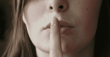 Mulher com o dedo na frente da boca, em sinal de silêncio