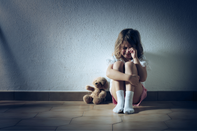 Menina sentada na parede de um corredor chorando