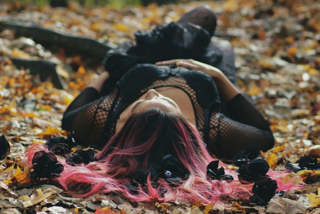 Mulher deitada no chão coberto por folhas, de barriga para cima.