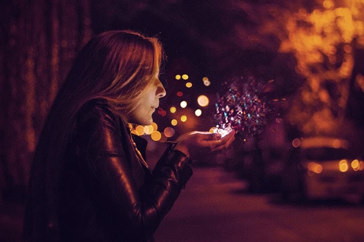 Mulher em uma rua, a noite, soprando das suas mãos glitters iluminados .