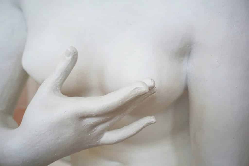 Detalhe de uma escultura de uma mulher com as mãos na frente dos seios.
