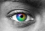 Foto preta e branca, próxima de olho humano, com a íris colorida com as cores do arco íris.