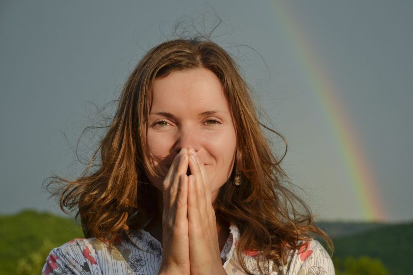 Mulher agradecendo. Com as mãos em sinal de oração. Fundo de arco-íris.