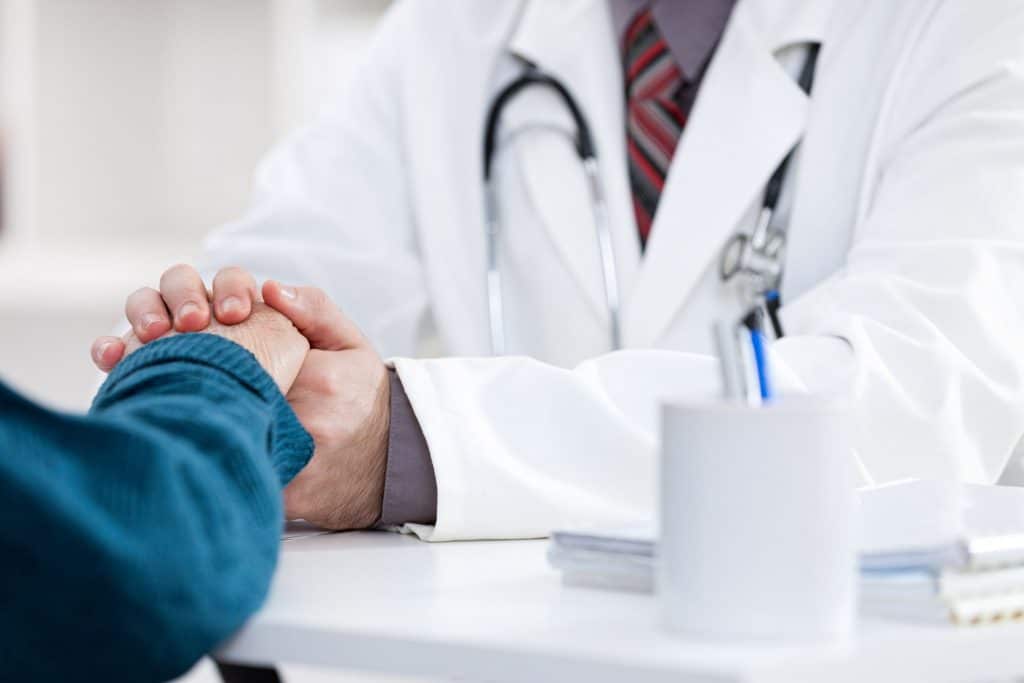 Homem médico segurando a mão do paciente.