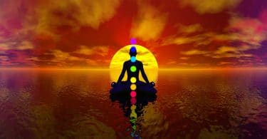 Desenho gráfico de um homem em meditação. Chakras representados como bolas coloridas. Fundo de pôr-do-sol e mar.