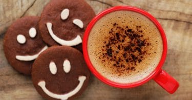 copo vermelho brilhante de espumoso café com biscoitos de chocolate com sorrisos feitos de chocolate branco.