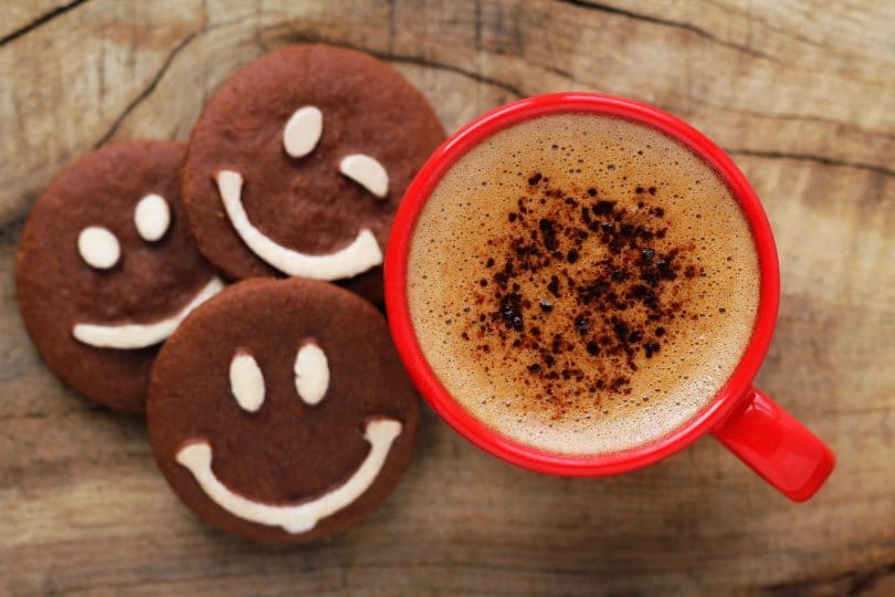 copo vermelho brilhante de espumoso café com biscoitos de chocolate com sorrisos feitos de chocolate branco.