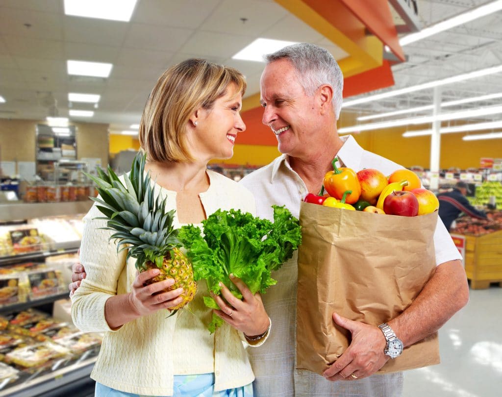 Casal adulto no supermercado segurando sacola com vegetais.