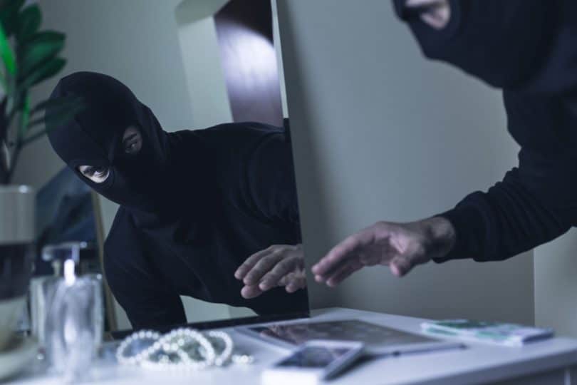 Bandido vestido um mascara de esqui preta, roubando jóias da cômoda de um quarto