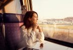 Mulher jovem sentada, viajando em trem, olhando para a janela.