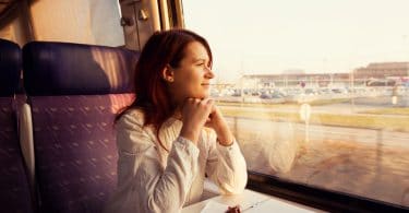 Mulher jovem sentada, viajando em trem, olhando para a janela.