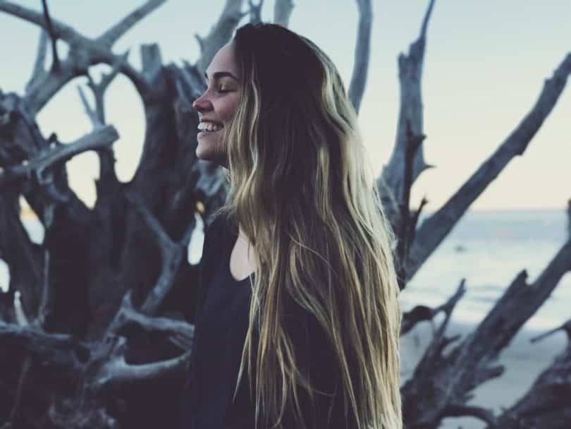 Jovem branca sorrindo com os olhos fechados.