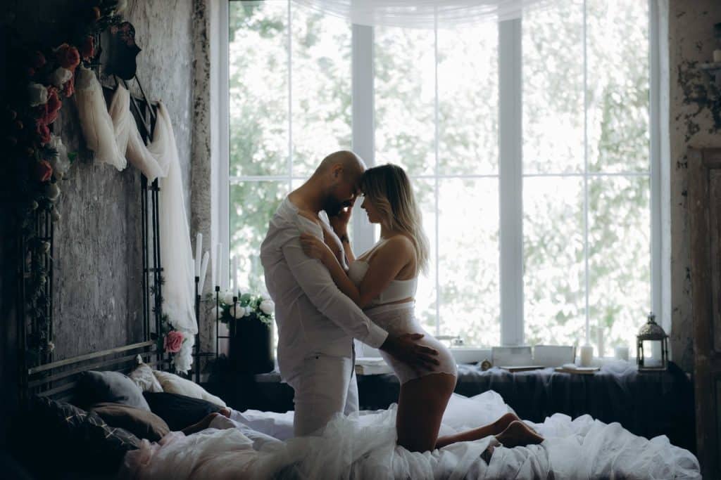 Homem e mulher de joelhos na cama, abraçados.