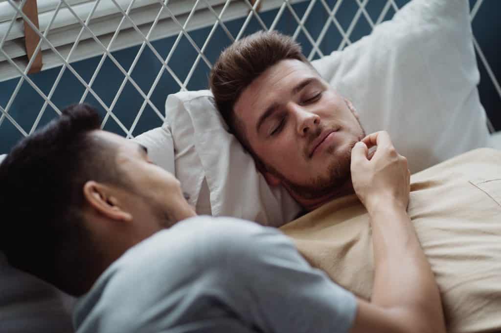 Homem acariciando o rosto de seu parceiro com ambos deitados na cama.