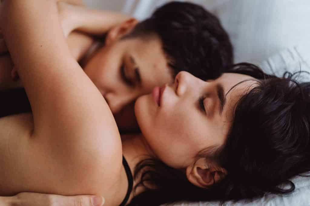 Duas mulheres abraçadas na cama, de olhos fechados.