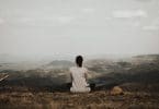 Mulher sentada na beira de uma montanha , em posição de meditação, observando o horizonte.