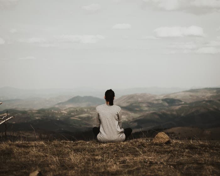 Mulher sentada na beira de uma montanha , em posição de meditação, observando o horizonte.