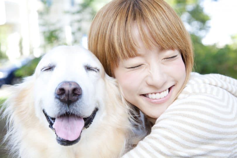 Garota asiática sorrindo e abraçando um cachorro.