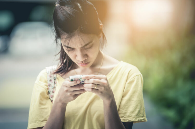 Menina asiática mexendo no celular com cara de séria.