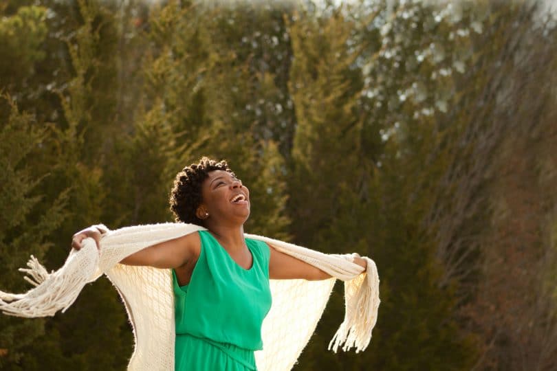 Mulher negra com braços abertos em um cenário de natureza e ar fresco.