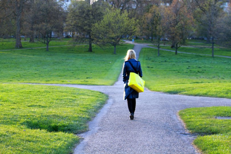 Mulher caminhando em uma estrada que está se dividindo em três novos caminhos.