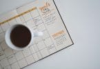 Agenda mensal com planejamento e listas de metas, em cima de uma mesa branca e com uma xícara de café.
