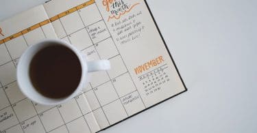 Agenda mensal com planejamento e listas de metas, em cima de uma mesa branca e com uma xícara de café.