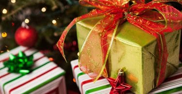 Presentes embrulhados, empilhados ao pé de uma árvore de natal decorada.
