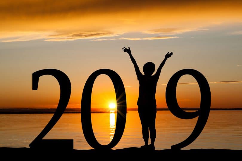 A silhueta 2019 do ano novo de uma menina com mãos levantadas, ocupando o lugar do 1 , na praia durante o nascer do sol dourado.