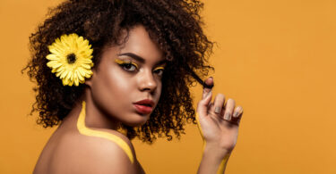 Mulher negra com uma flor amarela no cabelo.